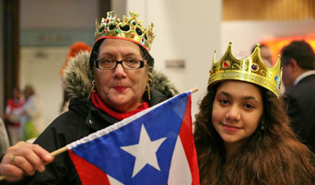 A woman and a girl wearing paper crowns holding a Puerto Rican flag