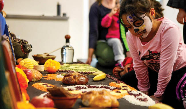 A girl with face paint looking at a Dia de los Muertos altar