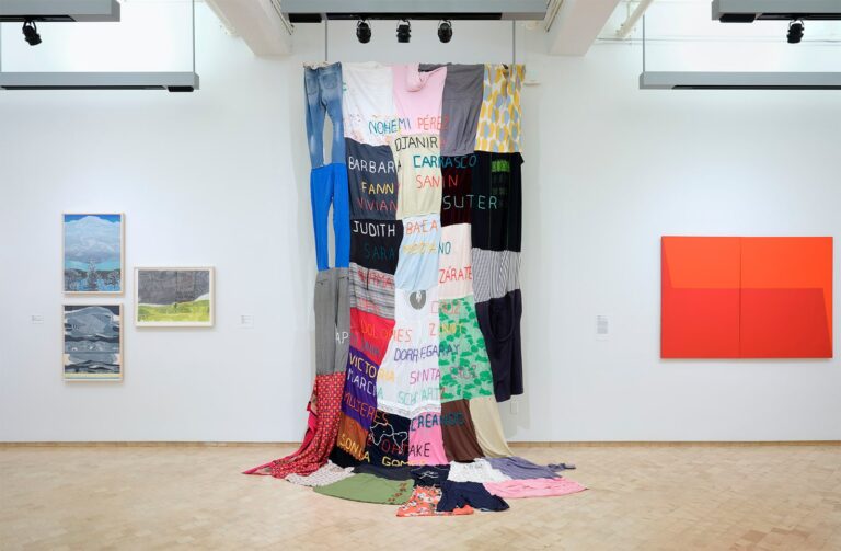 Carolina Caycedo. Muxeres en mi, 2019. Clothing and embroidery, 144 x 72 in. Gift of the Acquisitions Committee, 2022. Installation view at Something Beautiful: Reframing La Colección, El Museo del Barrio, 2023. Also displayed works by Myrna Báez (left) and Carmen Herrera (right). Photo On White Wall.