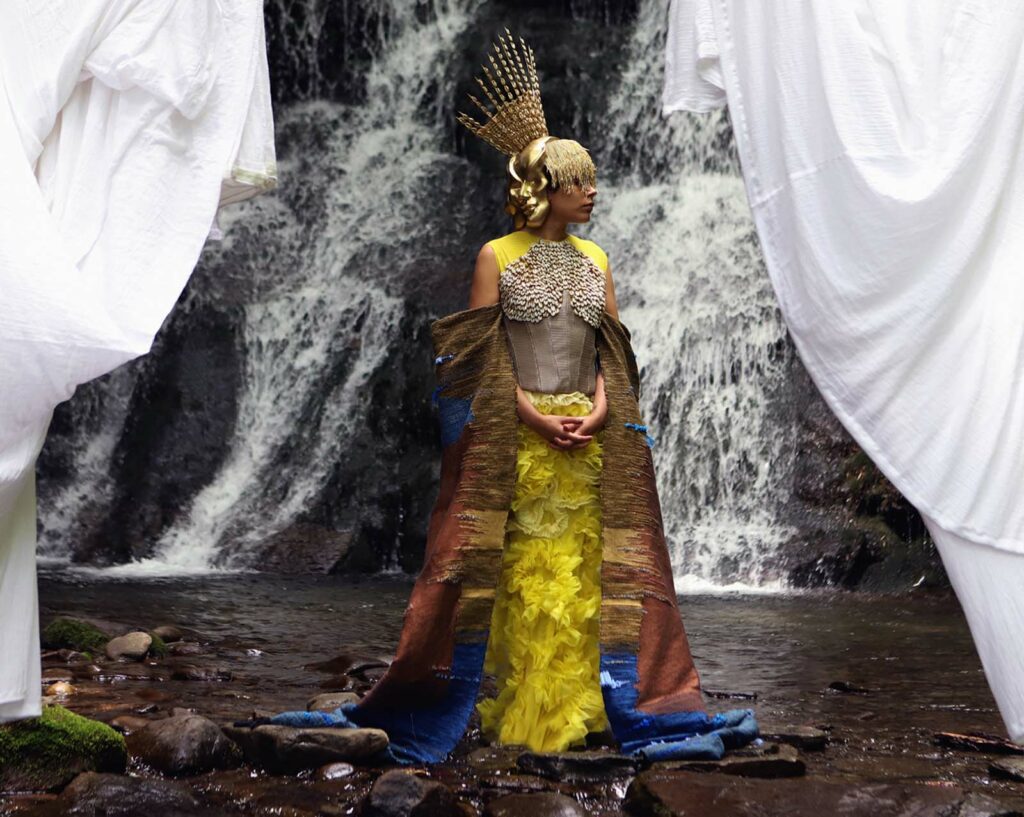 Goddess of fertility embodied by fellow Dominican artist Patricia Encarnación. Rodriguez created a marigold-colored gown adorned with cowrie shells, a brown-and-blue cape reflecting the Atlantic Ocean, and a three-pointed crown evoking symbolic three-pointed stones called trigonolitos, found in Caribbean Taíno material culture.