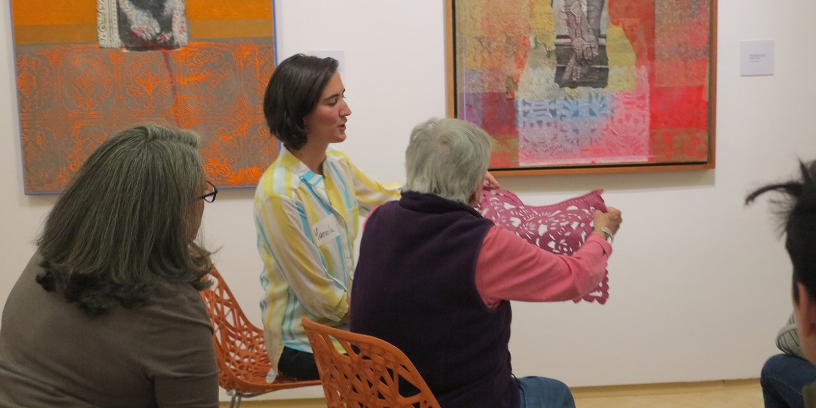 Group of people in an art gallery, focusing on a woman (center) holding up a piece of paper art