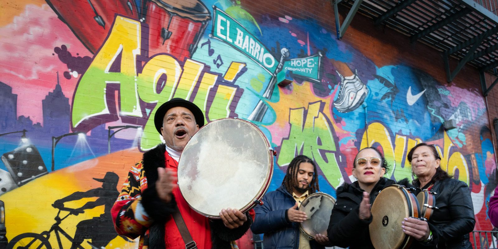 A group of people are playing music in front of a colorful graffiti wall.